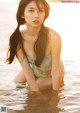 A woman in a bikini sitting in the water.