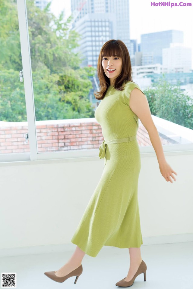 A woman in a green dress standing in front of a window.