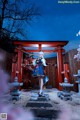 A woman in a blue and white dress standing in front of a red gate.