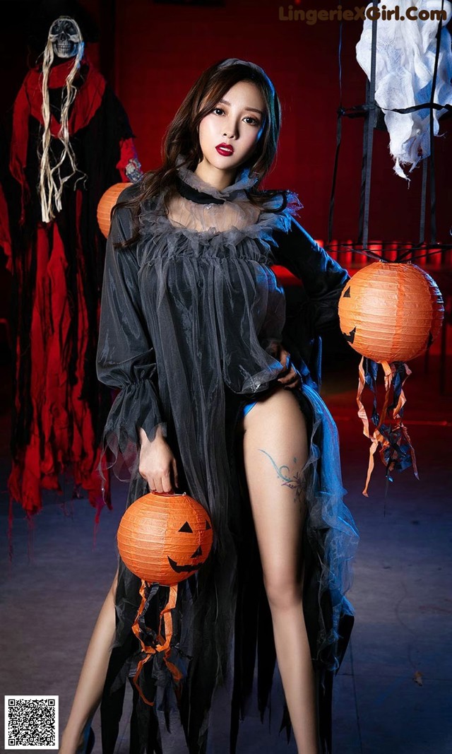 A woman in a black dress holding a pumpkin.